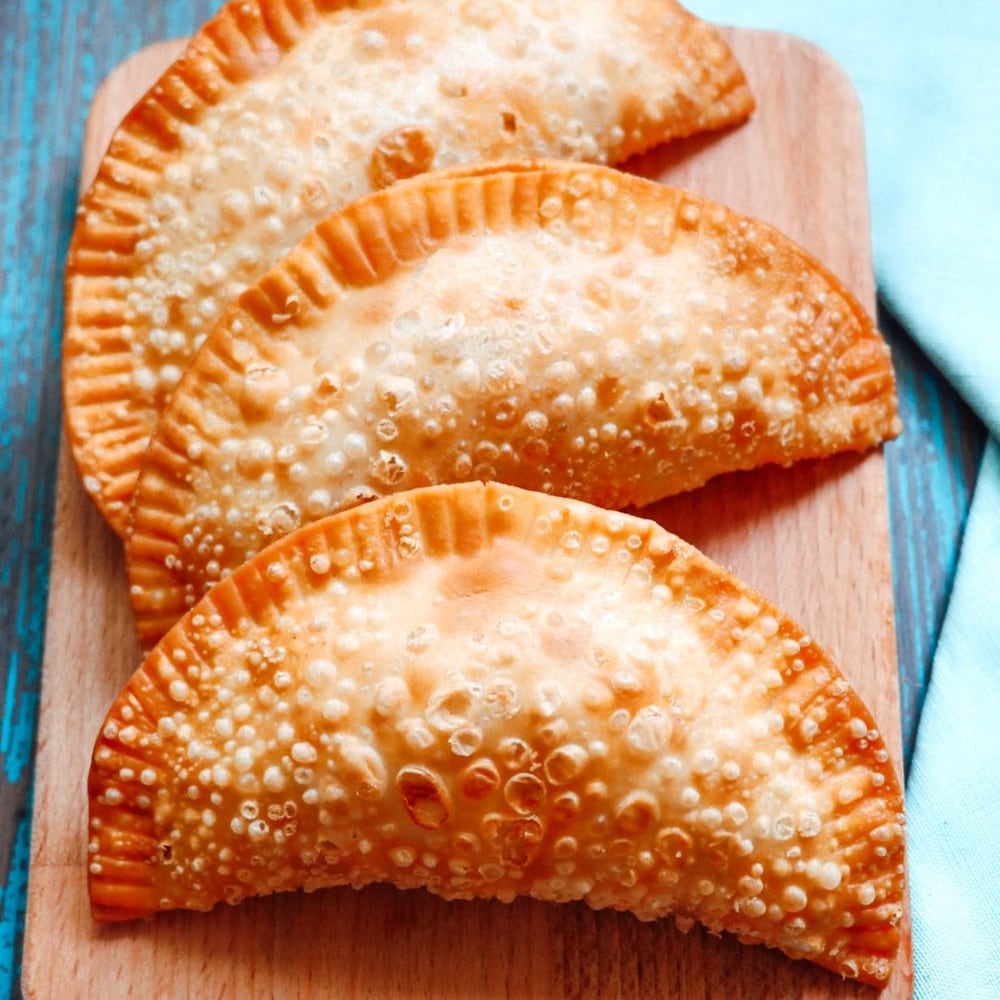 Three fried empanadas on a wooden board.