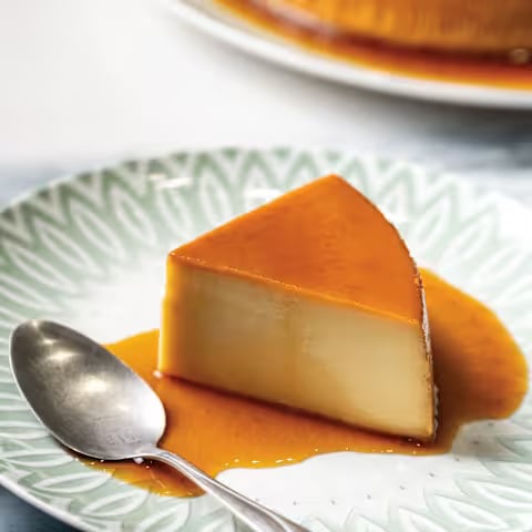 A slice of flan with caramel sauce and a spoon on a patterned plate.